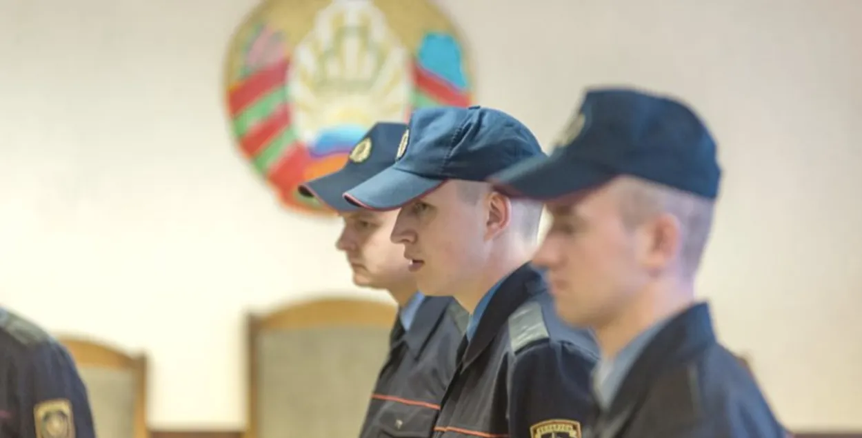 Міліцыянеры на фоне дзяржаўнага герба Беларусі
