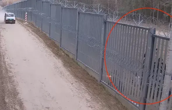 В просветах в заборе виден человек в форме цвета хаки
